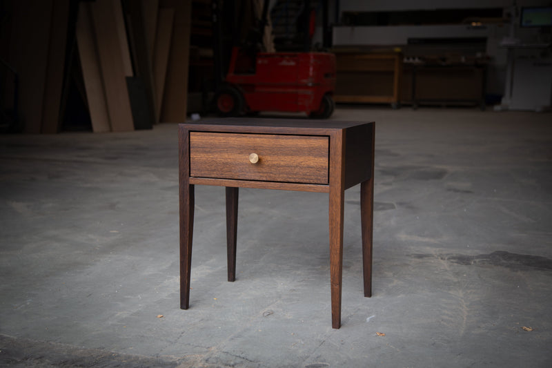Snedkerlavet sengebord i røget eg med en enkelt skuffe og messinggreb
